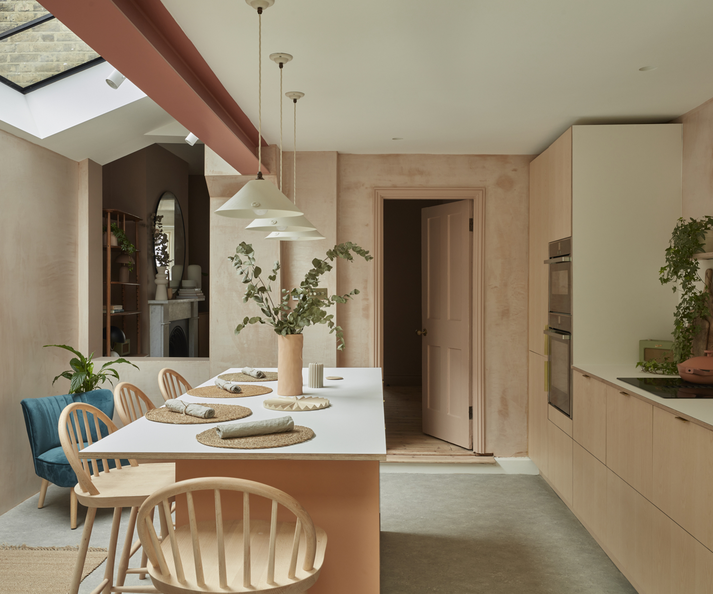 A new kitchen extension full of natural light, with raw plaster walls, concrete effect flooring, plywood units and a pop of terracotta