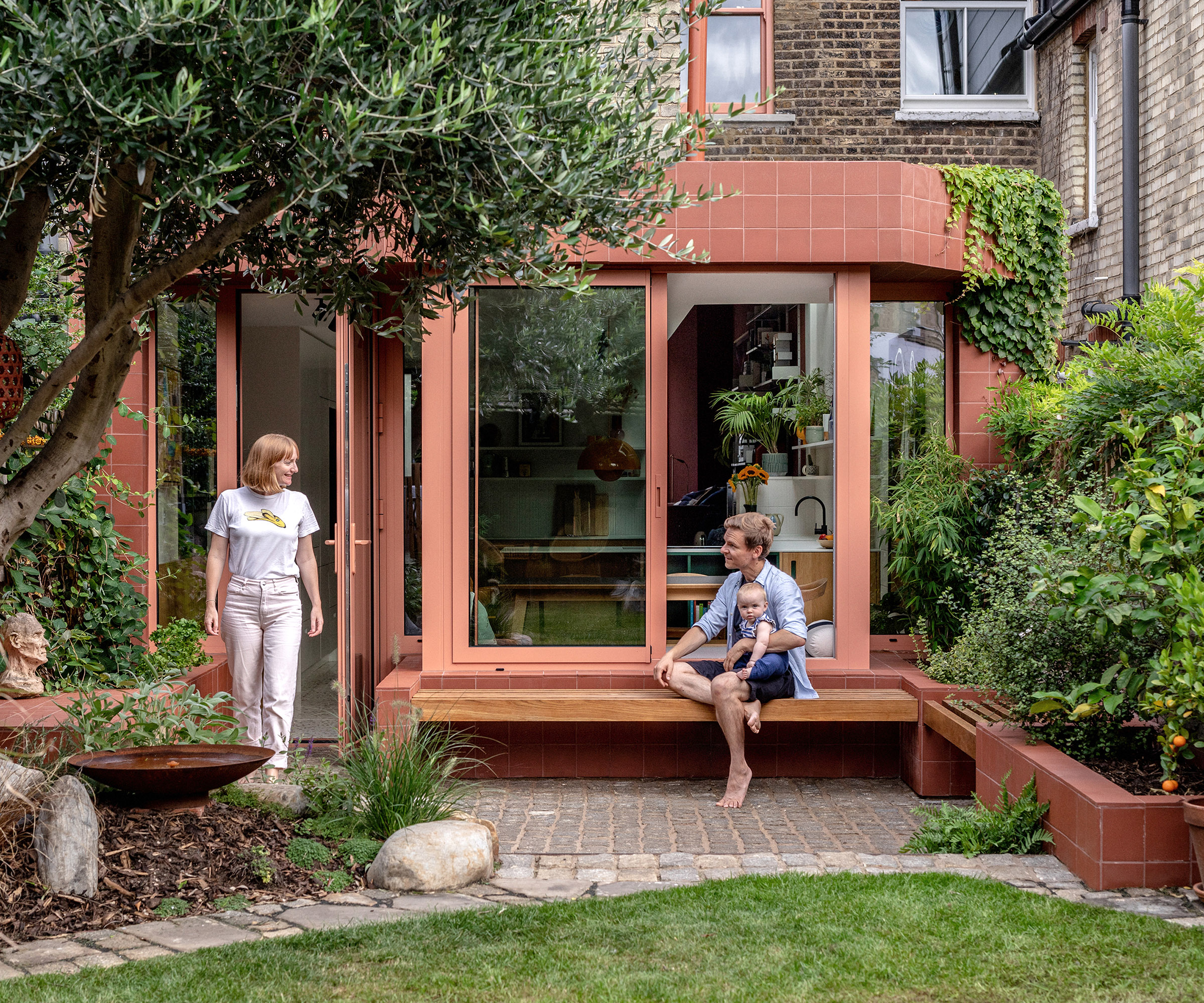 A modern extension of a london terraced house clad in terracotta colour materials with a young family enjoying the space