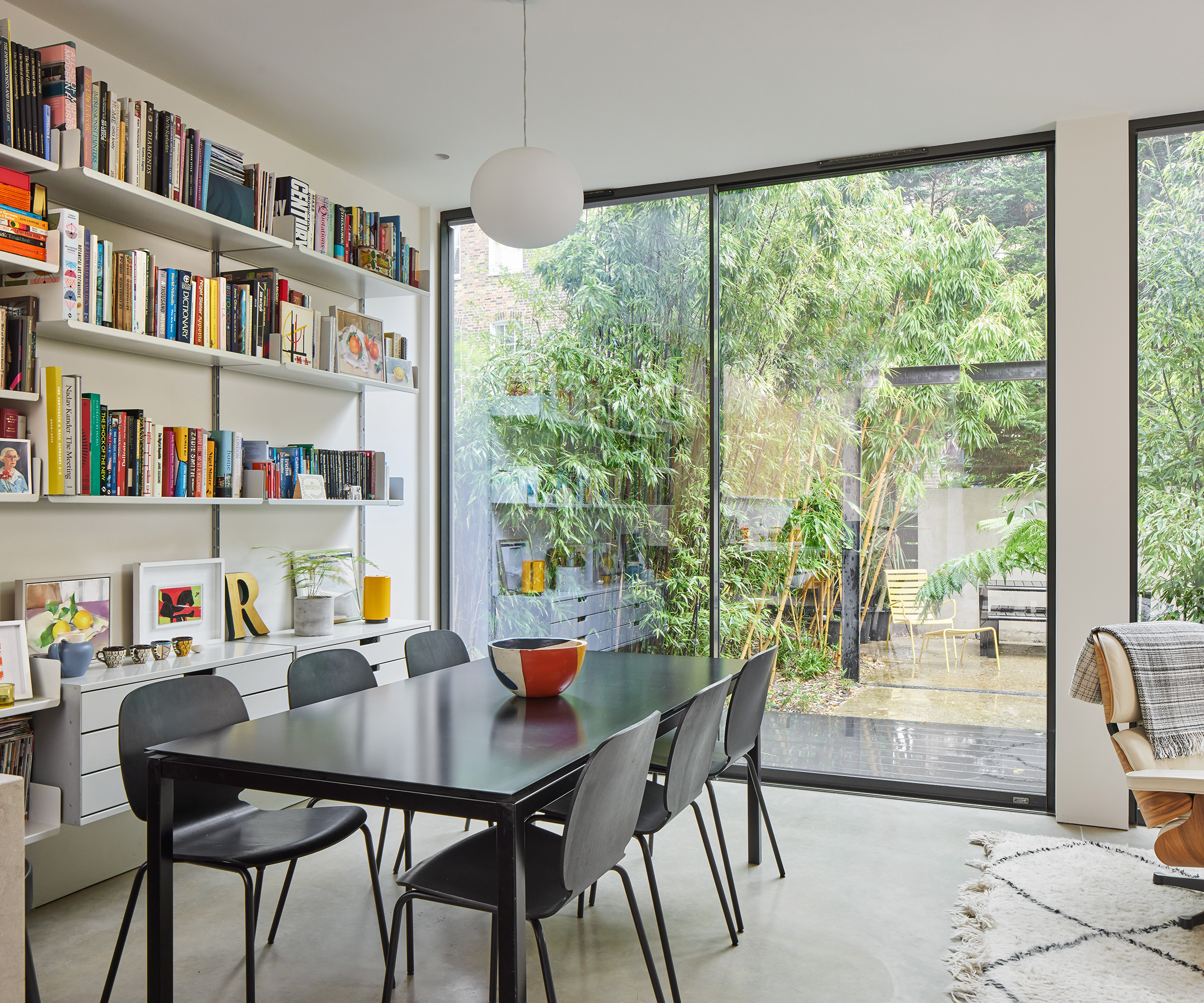 A black dining table on a polished concrete floor with colourful bookshelves and large sliding glass doors